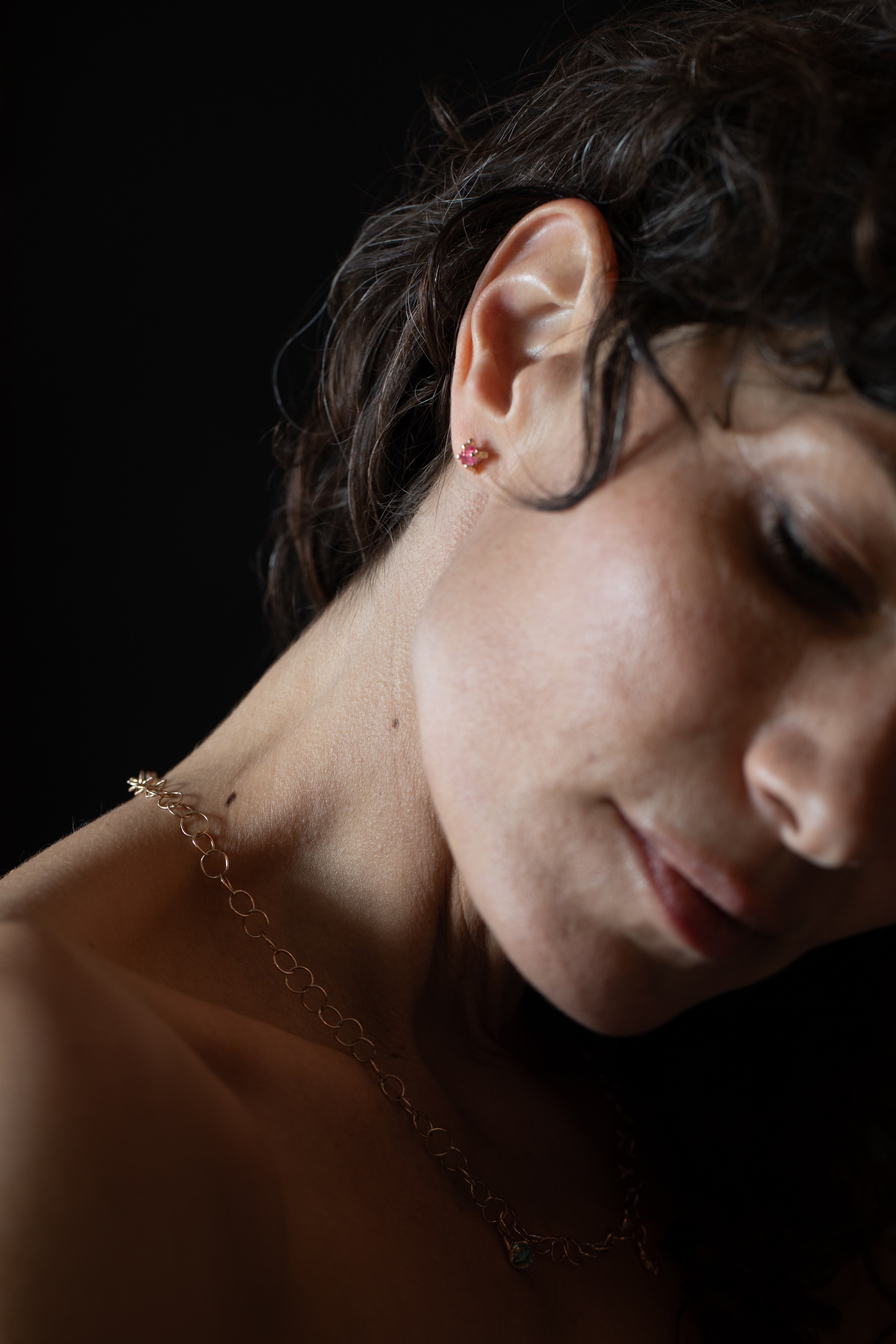 Close-up of a spinel earring and gold chain against a dark background