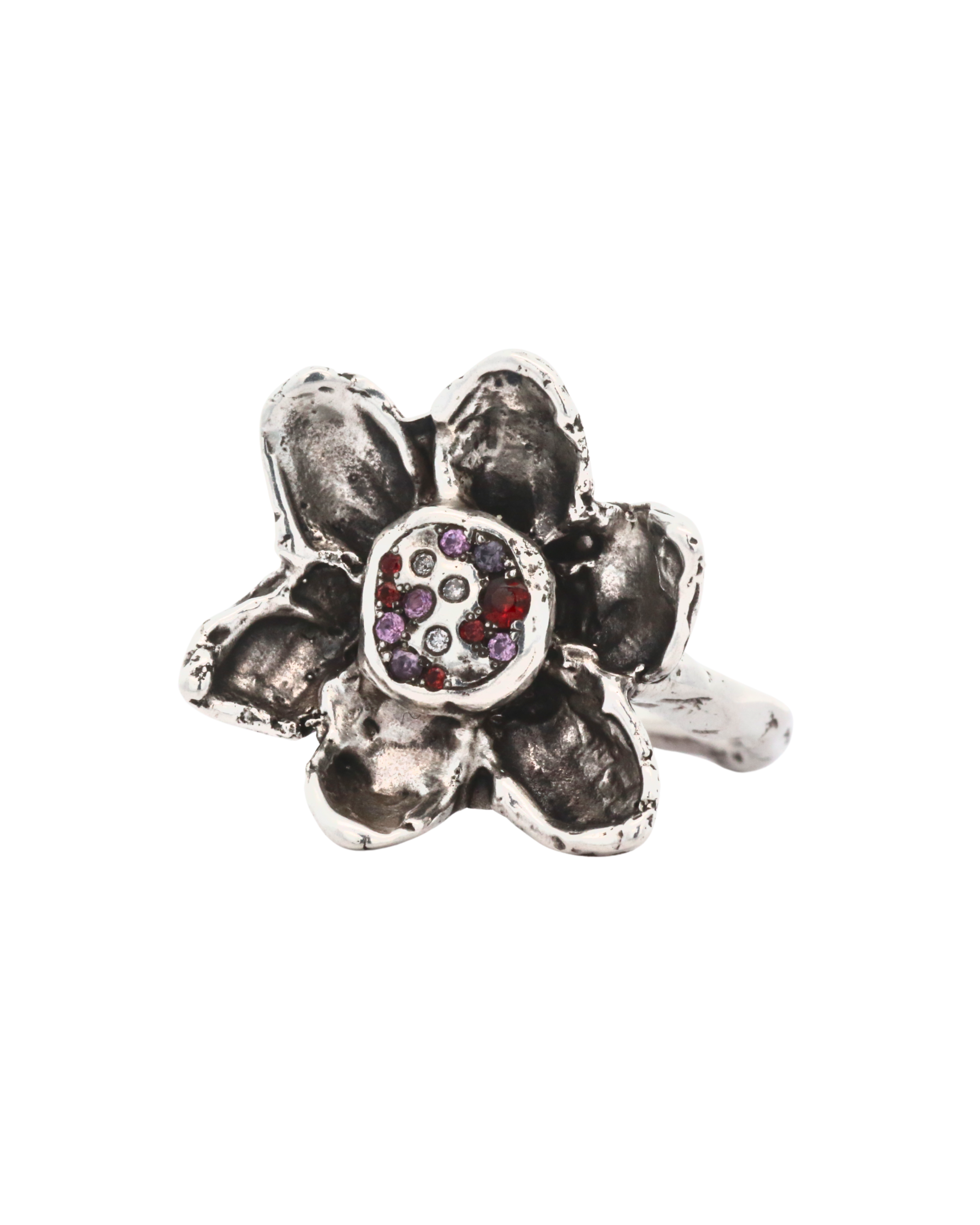 A silver-toned flower ring with textured petals and a central cluster of small gemstones in red, purple, and clear, shown on a plain white background.